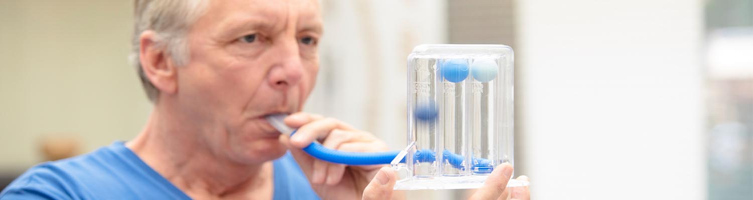 older man in blue t-shirt breathing into a tube connected to a spirometer